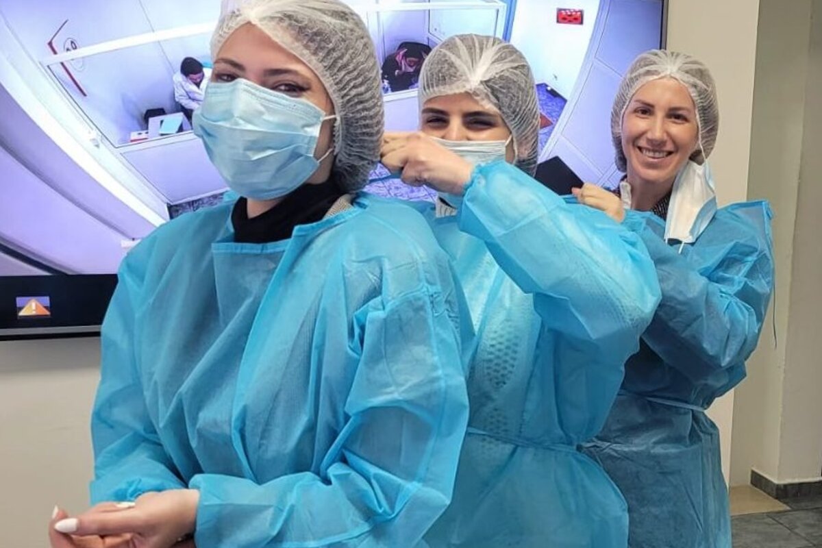 Three food safety specialists in gowns, hairnets and masks preparing to enter a production area.